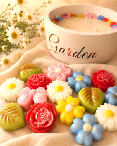 Bombones de cera en forma de flores de colores con vela aromatica de fondo